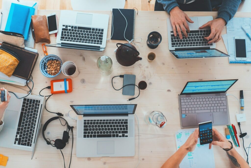 Estação de trabalho com notebooks abertos, mãos no teclado e materiais de escritório sobre a mesa